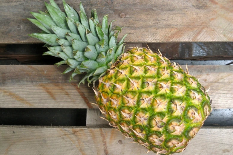 Zrálý ananas s zelenou korunou na dřevěném povrchu.