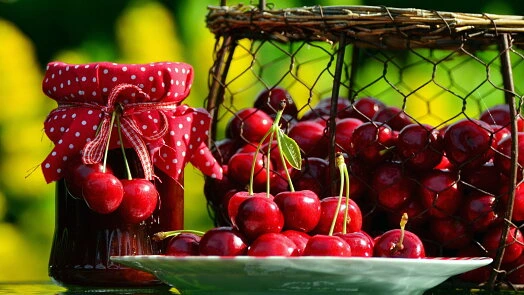 Sklenice třešňové marmelády vedle košíku čerstvých třešní.