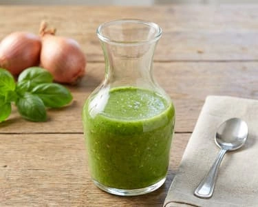 Sklenice zeleného bazalkového pesto s čerstvou bazalkou.