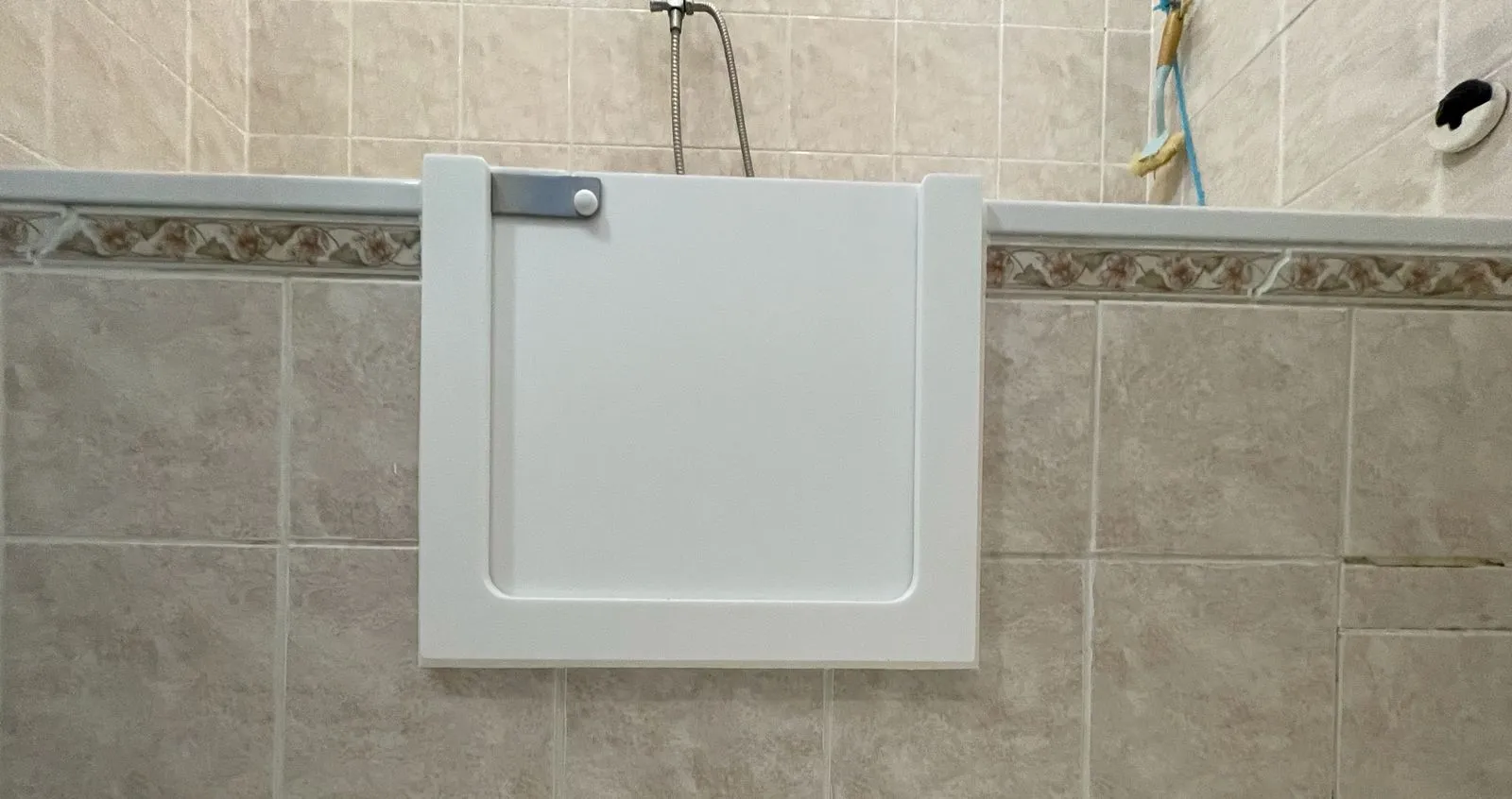 Bílá dveřka do vany nainstalovaná na okraji vanové mísy.