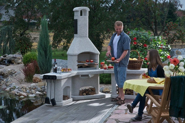 Muž stojí u velké betonové zahradní grilu s kouřovnou.
