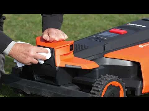 Člověk čistí robotickou sekačku na trávu hadříkem.