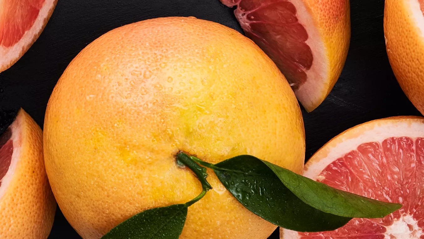Celý pomerančový citrus s listy a řezané plátky na tmavém pozadí.