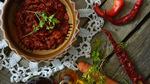 Domácí ajvar v misce s čerstvými paprikami a kořením